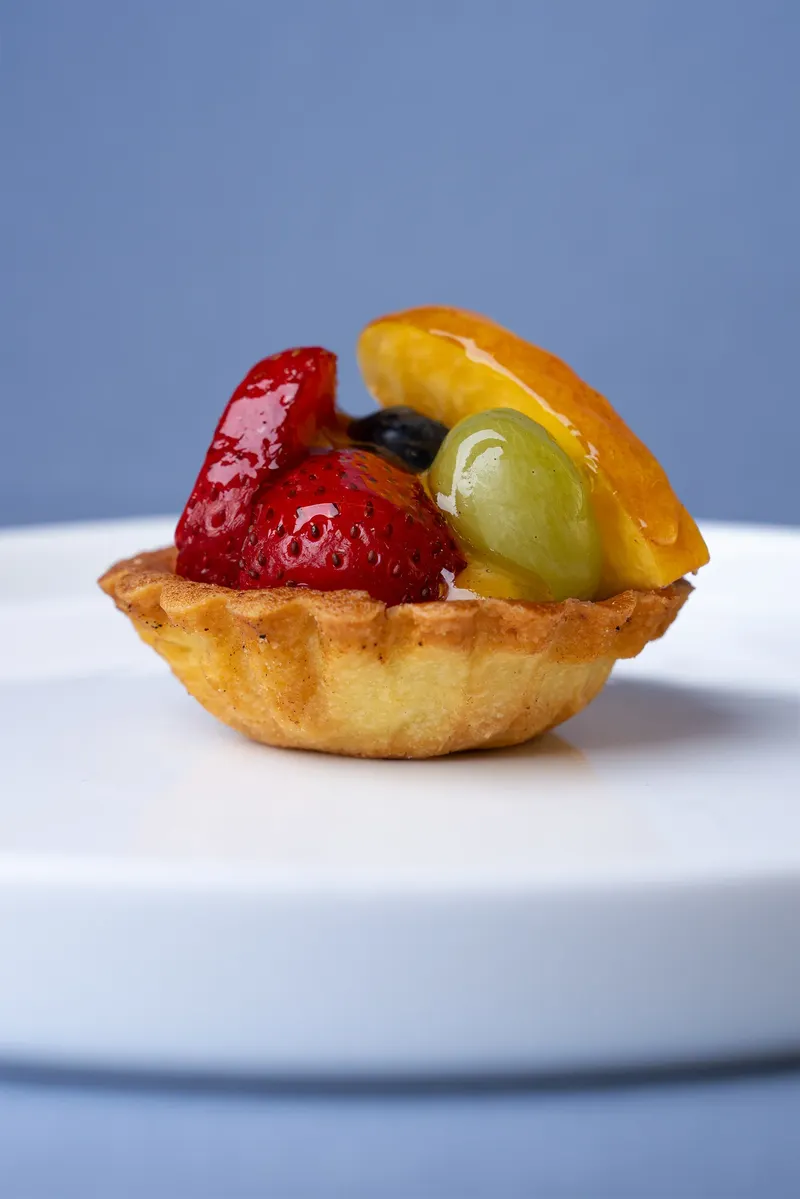 Crostatina con fragola, uva e arancia su fondale blu